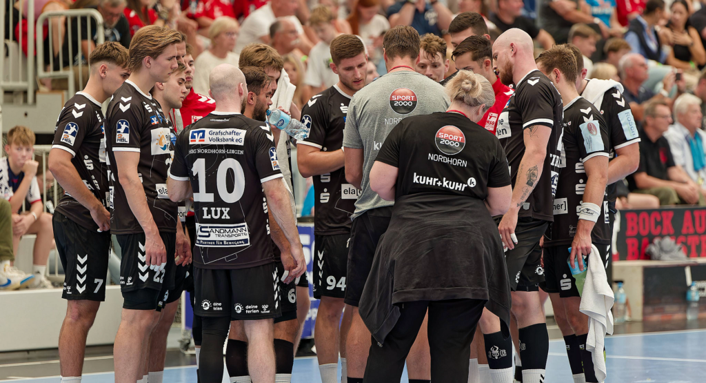 Das Bild zeigt die Mannschaft der HSG Nordhorn, wie sie in der Pause zusammen in einem Kreis stehen und sich besprechen.