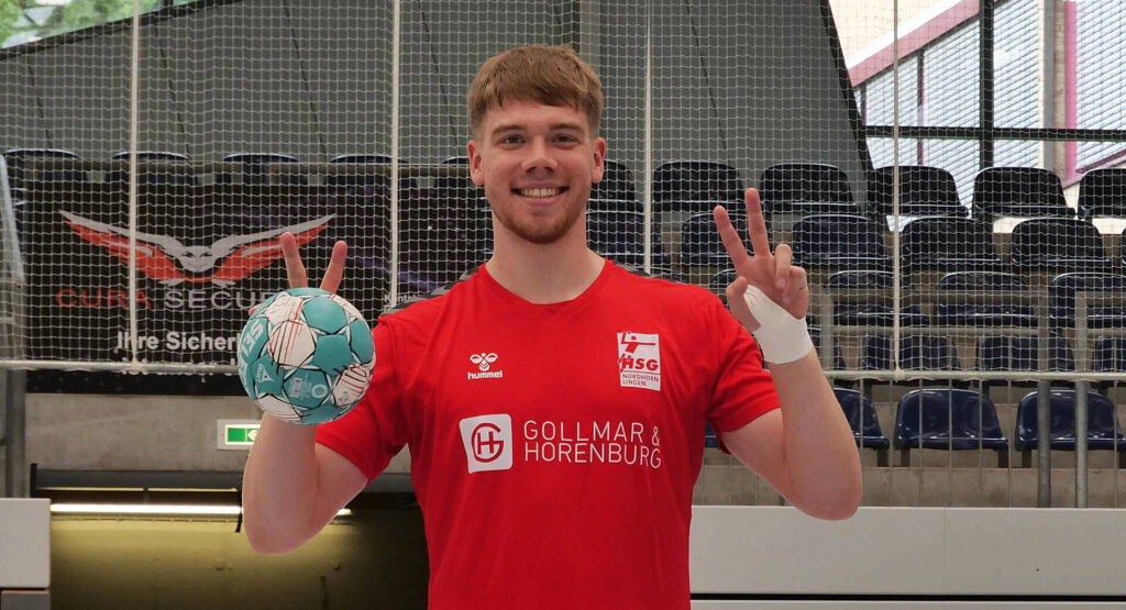 Das Bild zeigt Elias Ruddat, erhält einen Handball in der Hand und zeigt das "Peace" Zeichen.