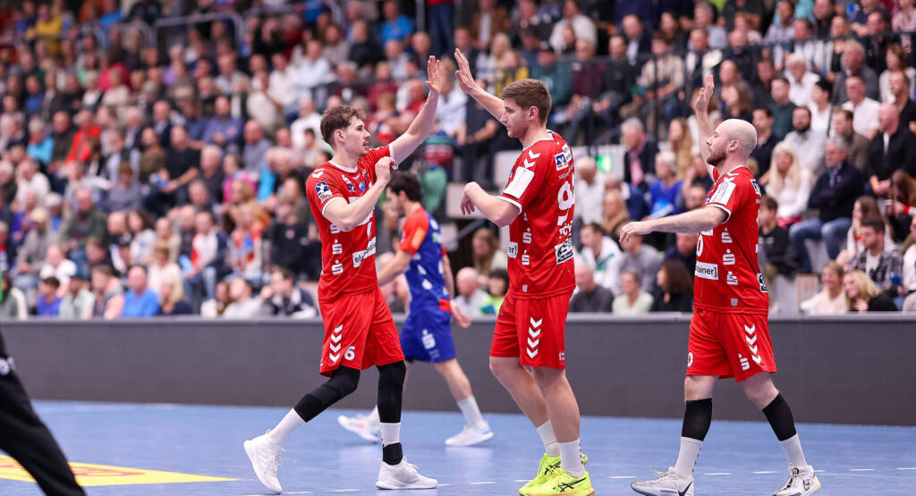 Das Bild zeigt drei Spieler der HSG Nordhorn-Lingen, die sich gegenseitig Abklatschen.