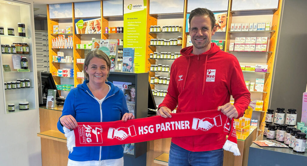 Das Bild zeigt die Inhaberin der Apotheke am Postdamm, Katja Reynolds und einen Mann stellvertretend für die HSG. Sie halten beide einen Fanschal hoch, in der Mitte steht "HSG Partner".