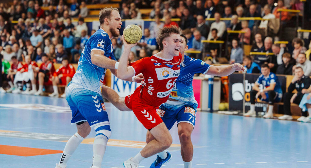 Das Bild zeigt einen Handball Spieler der HSG der von 2 Gegenspielern versucht wird beim Torwurf geblockt zu werden.