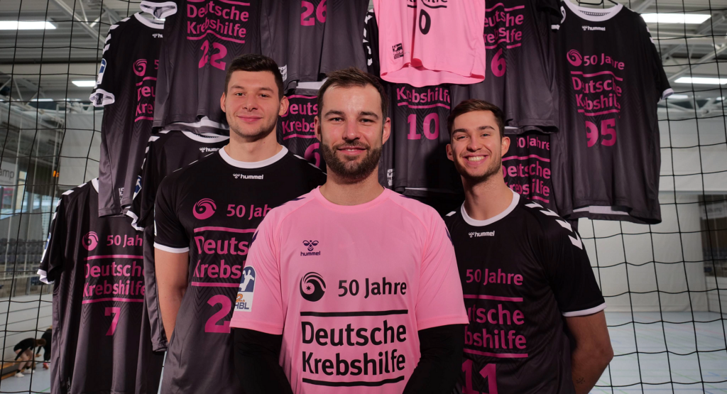 Das Bild zeigt 3 Spieler der HSG Nordhorn-Lingen. Sie sind alle in Sondertrikots gekleidet, für "50 Jahre, Deutsche Krebshilfe".