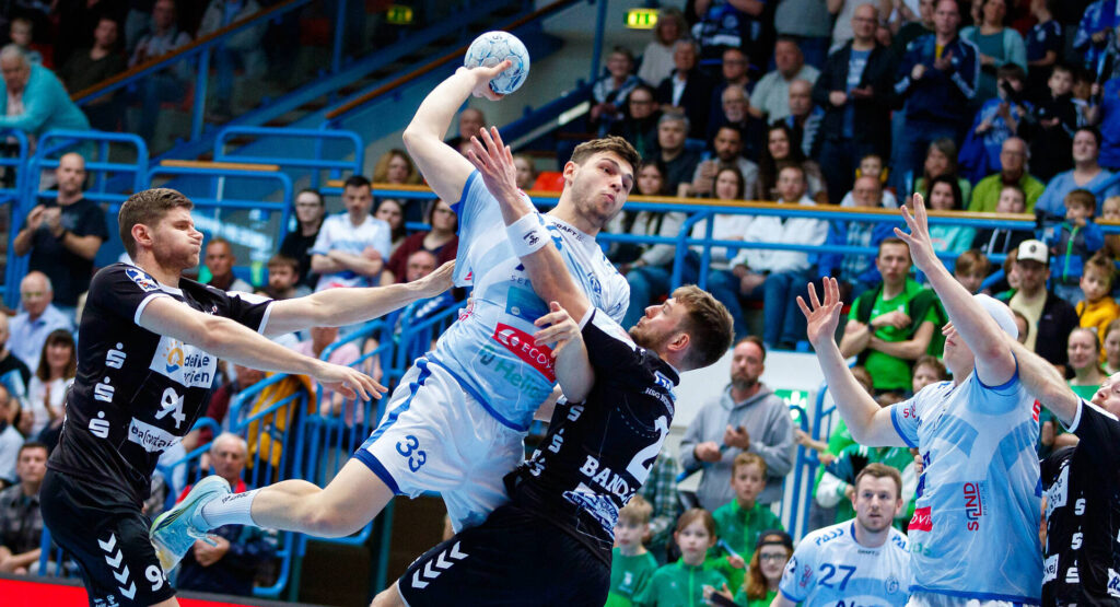 Das bild zeigt die Nummer 33 von Großwallstadt, wie er von zwei HSG-Spielern versucht wird zu blocken.